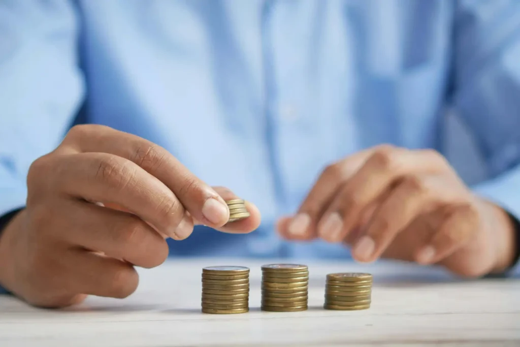 Person, die Münzen stapelt, um das Sparen und den Umgang mit Geld darzustellen.