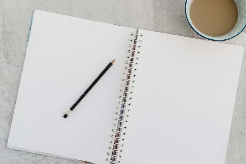 Un cuaderno abierto con un lápiz y una taza de café sobre la mesa, representando las opciones de franquicia en el seguro de salud suizo para 2025.